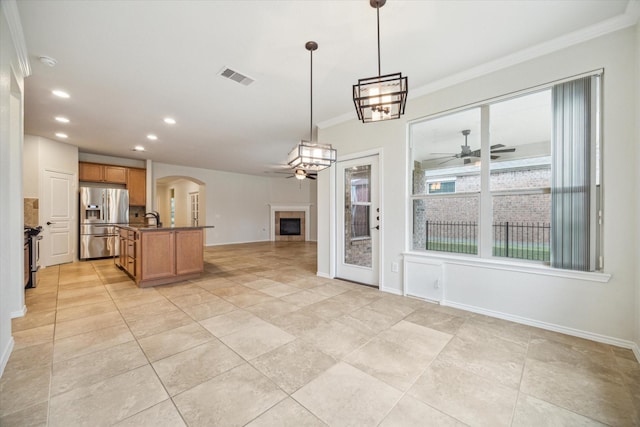 kitchen featuring decorative light fixtures, ornamental molding, ceiling fan, stainless steel fridge with ice dispenser, and a center island with sink