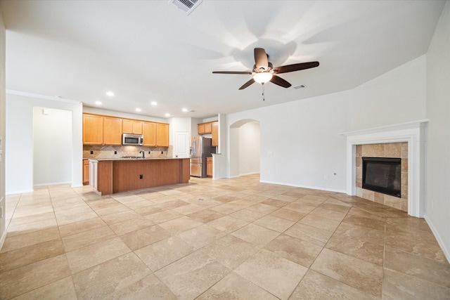 unfurnished living room featuring baseboards, visible vents, arched walkways, ceiling fan, and a tiled fireplace