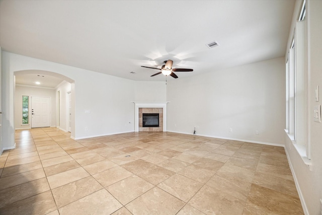 unfurnished living room with visible vents, baseboards, ceiling fan, a tiled fireplace, and arched walkways