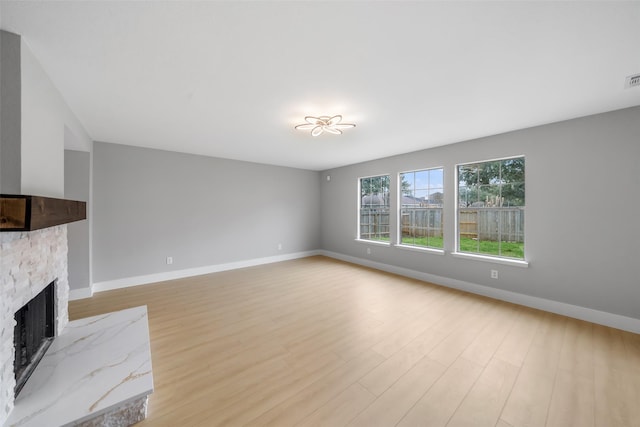 unfurnished living room featuring a stone fireplace and light wood-type flooring