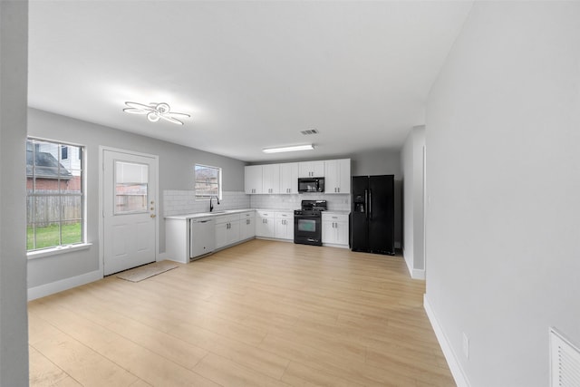 kitchen with white cabinetry, black appliances, light wood-type flooring, plenty of natural light, and backsplash