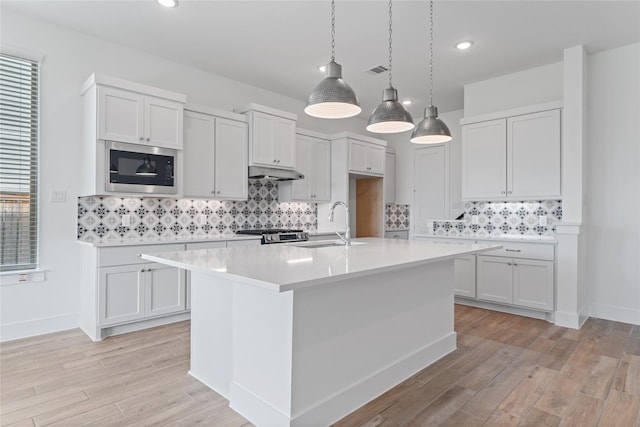32646 Fly Fish Way, Fulshear, TX 77441 - kitchen with stainless steel microwave, a sink, light countertops, under cabinet range hood, and light wood-style floors