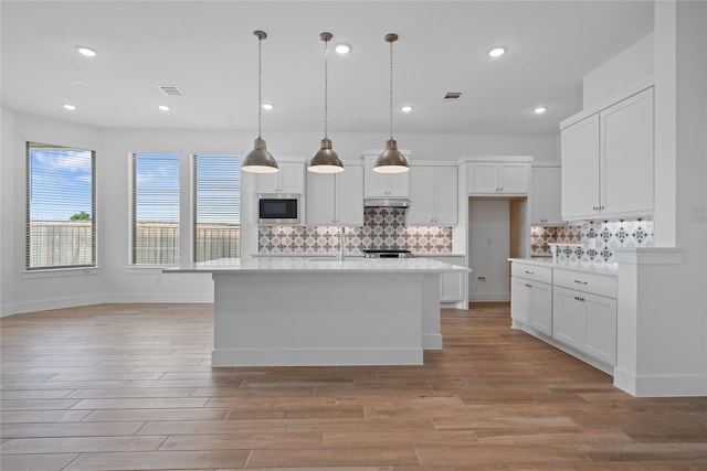 32646 Fly Fish Way, Fulshear, TX 77441 - kitchen featuring stainless steel microwave, light wood finished floors, light countertops, tasteful backsplash, and white cabinets