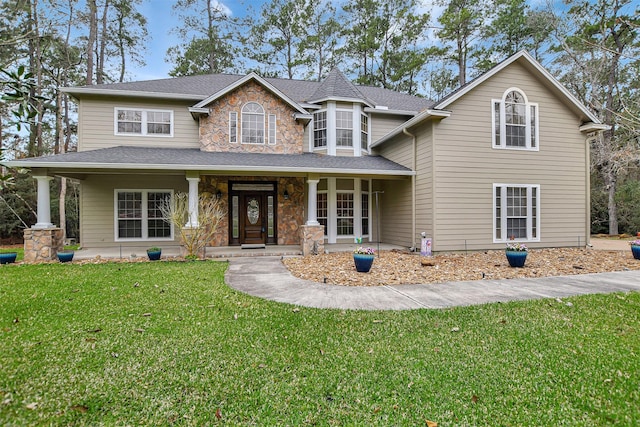 view of front facade featuring a porch, a front yard, stone siding, and roof with shingles