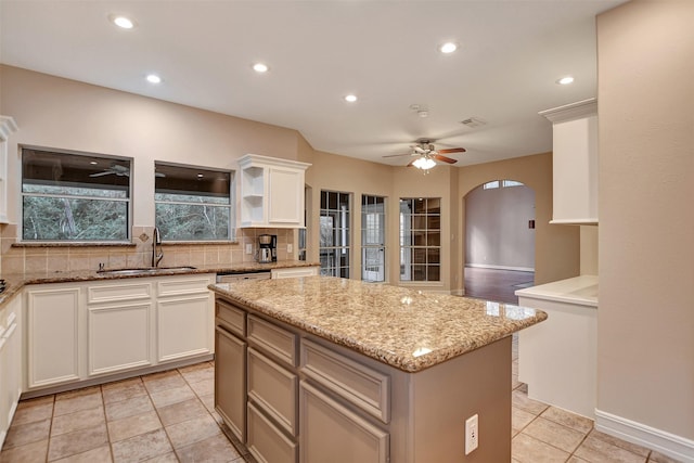 kitchen with decorative backsplash, a kitchen island, a sink, arched walkways, and ceiling fan