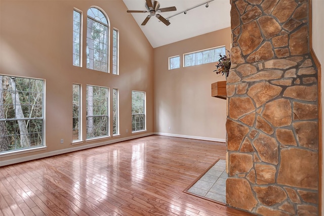 unfurnished living room with wood-type flooring, high vaulted ceiling, baseboards, and ceiling fan