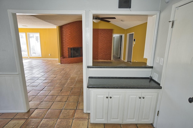 kitchen with white cabinets, vaulted ceiling, a brick fireplace, and a textured ceiling