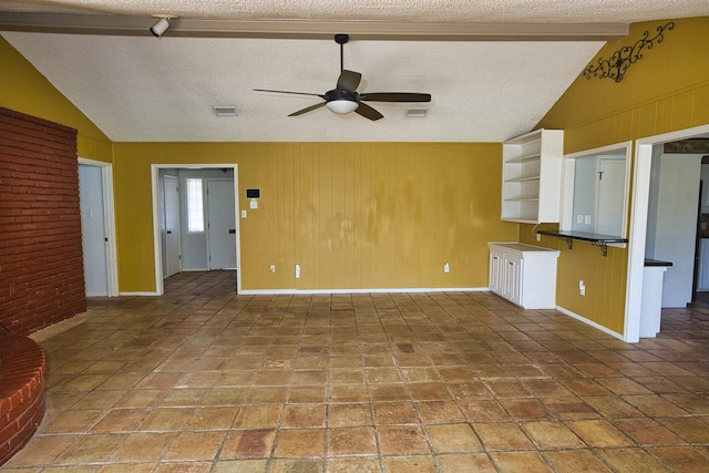 interior space featuring ceiling fan, vaulted ceiling with beams, wooden walls, and a textured ceiling