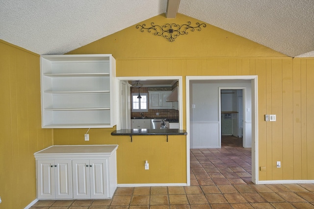 kitchen featuring wall chimney range hood, lofted ceiling with beams, stainless steel dishwasher, and a textured ceiling