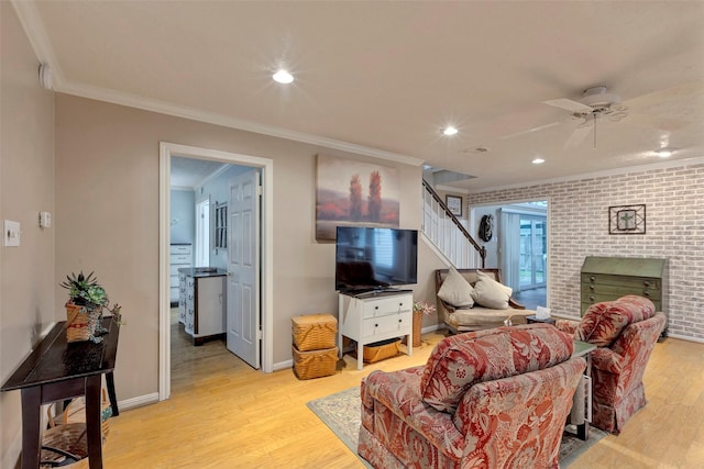 living room with brick wall, a fireplace, ceiling fan, crown molding, and light hardwood / wood-style flooring