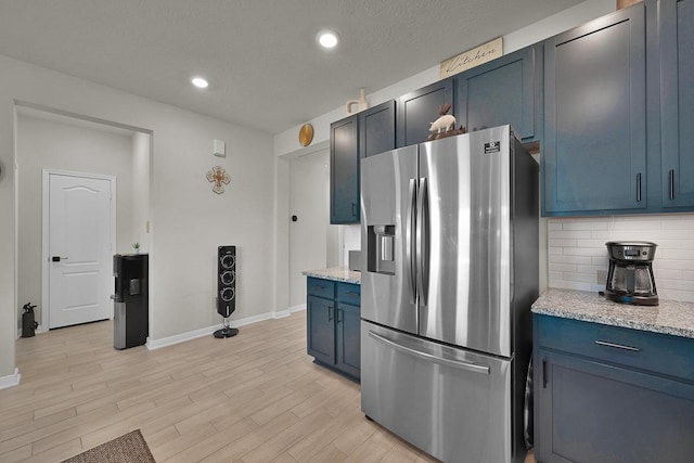 kitchen with stainless steel fridge, light hardwood / wood-style flooring, backsplash, light stone counters, and blue cabinets