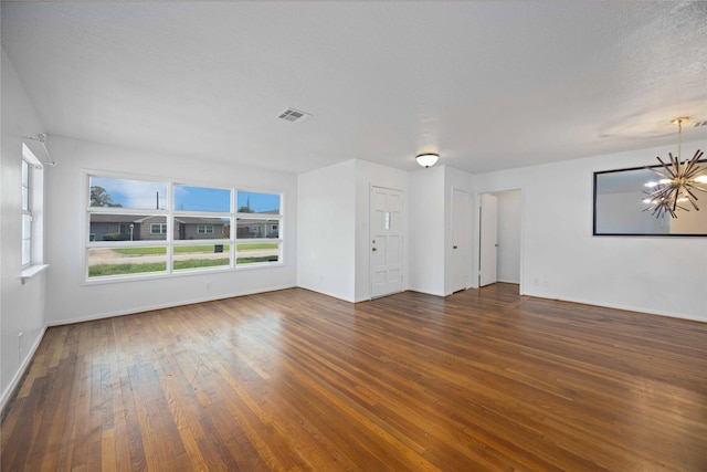 empty room with a textured ceiling, dark wood-type flooring, and an inviting chandelier