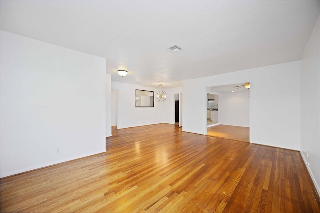 unfurnished room with ceiling fan with notable chandelier and light hardwood / wood-style flooring