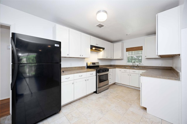 kitchen with stainless steel range with gas cooktop, black refrigerator, and white cabinetry