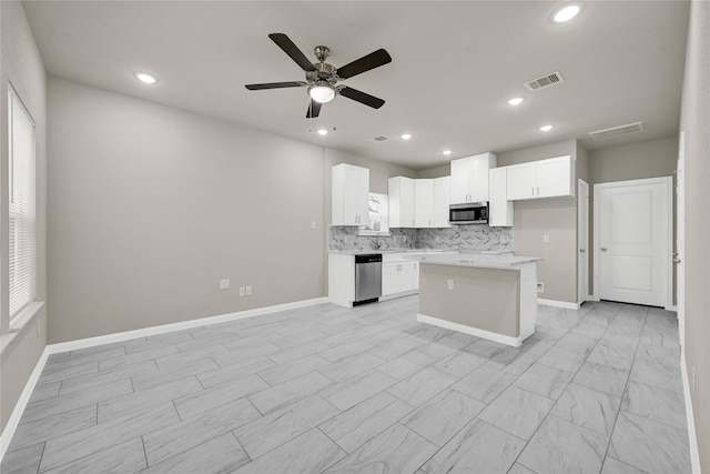 kitchen with tasteful backsplash, a kitchen island, ceiling fan, stainless steel appliances, and white cabinets