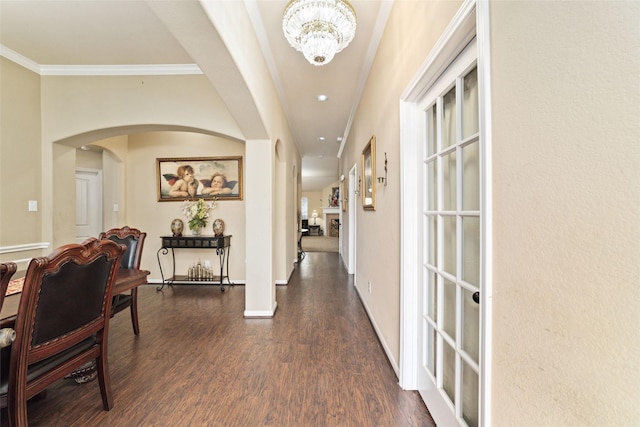 hall featuring arched walkways, crown molding, a notable chandelier, dark wood finished floors, and baseboards