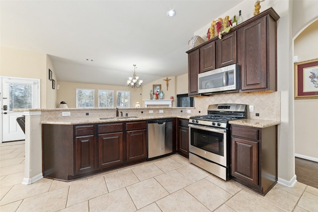 kitchen featuring dark brown cabinetry, stainless steel appliances, a peninsula, a sink, and backsplash