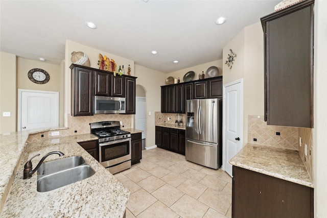 kitchen with arched walkways, light stone countertops, stainless steel appliances, a sink, and decorative backsplash