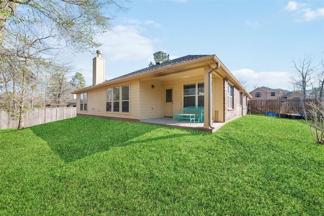 back of house featuring a fenced backyard, a chimney, a lawn, and a patio