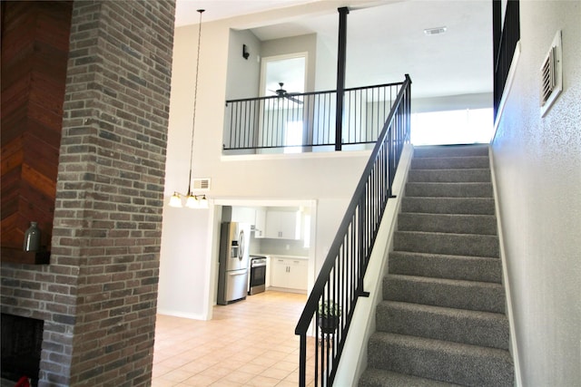 stairway with tile patterned flooring, a brick fireplace, a high ceiling, and ceiling fan