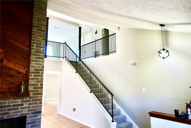 stairs with a fireplace, high vaulted ceiling, and a textured ceiling