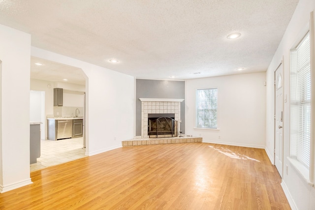 unfurnished living room featuring a tiled fireplace, sink, a textured ceiling, and light hardwood / wood-style floors