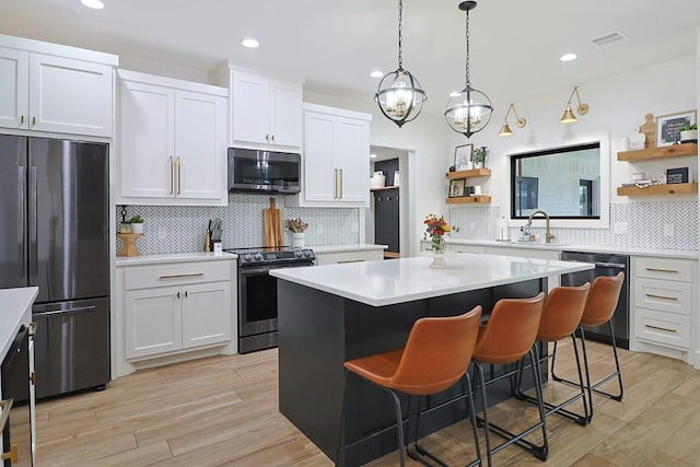 kitchen with appliances with stainless steel finishes, white cabinetry, a kitchen island, a kitchen bar, and light wood-type flooring