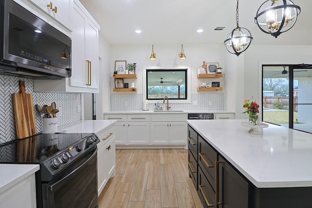 kitchen with black electric range oven, sink, decorative light fixtures, a kitchen island, and white cabinets