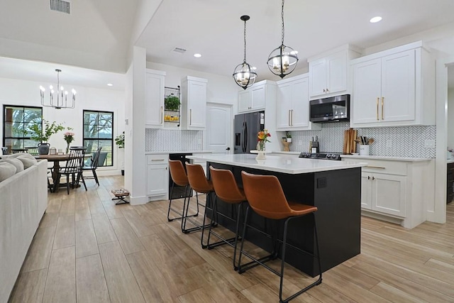 kitchen with white cabinetry, a center island with sink, stainless steel fridge, and a chandelier