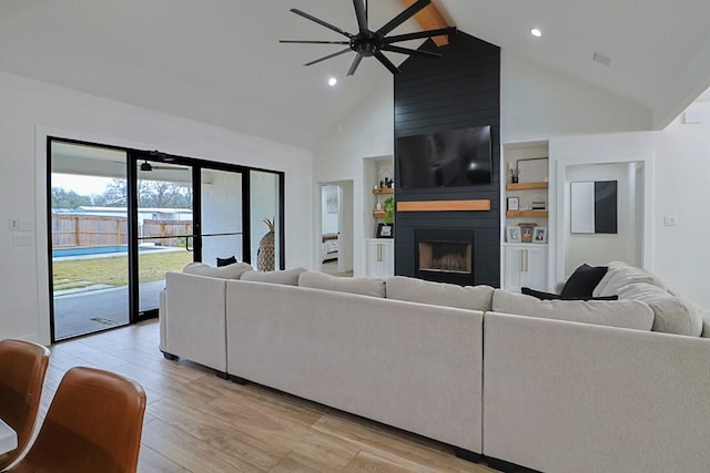 living room featuring high vaulted ceiling, a fireplace, light wood-type flooring, ceiling fan, and beam ceiling