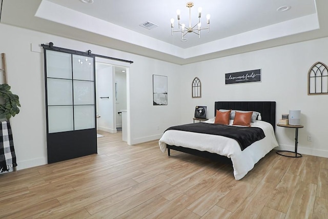 bedroom featuring a tray ceiling, light hardwood / wood-style flooring, a barn door, and a chandelier