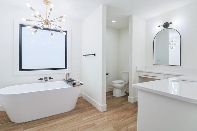 bathroom with a tub to relax in, toilet, an inviting chandelier, vanity, and hardwood / wood-style floors