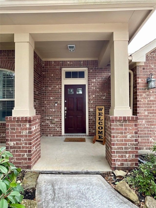 entrance to property featuring a porch and brick siding