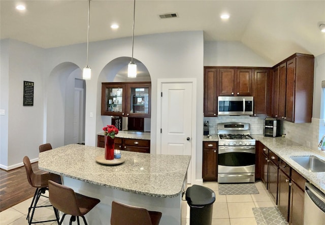 kitchen with light stone counters, stainless steel appliances, visible vents, hanging light fixtures, and backsplash