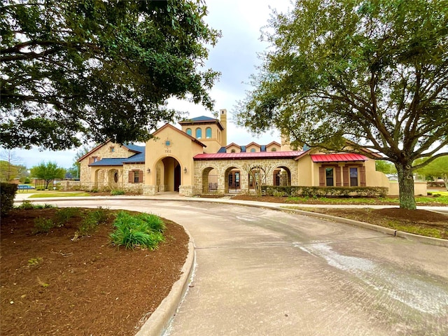 mediterranean / spanish house with stone siding, a chimney, concrete driveway, and stucco siding