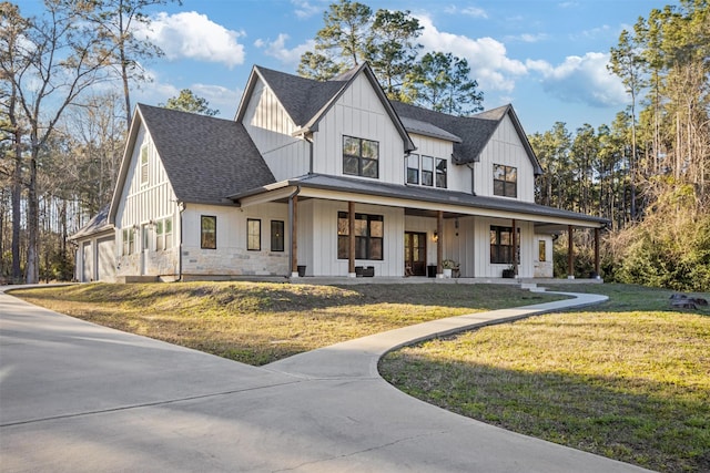 modern farmhouse style home featuring stone siding, roof with shingles, a porch, board and batten siding, and a front yard