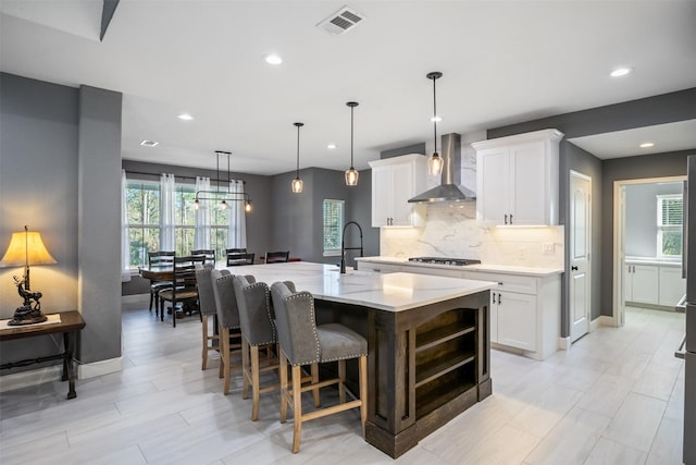 kitchen with visible vents, wall chimney exhaust hood, a sink, white cabinetry, and backsplash