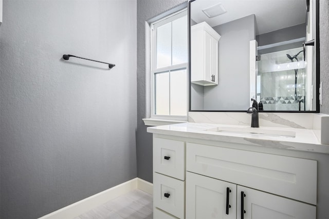 bathroom featuring baseboards, a textured wall, a shower stall, and vanity