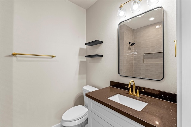 bathroom featuring vanity, a tile shower, and toilet