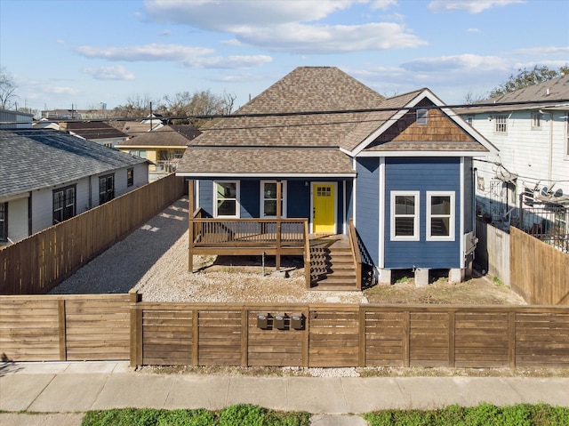 view of front facade with covered porch, roof with shingles, and a fenced backyard