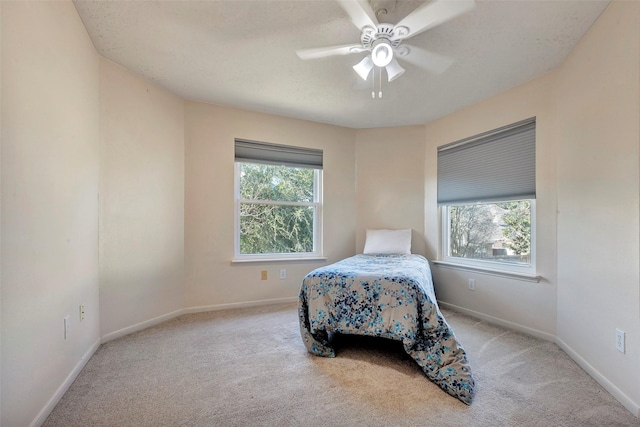 bedroom featuring light carpet, multiple windows, a ceiling fan, and baseboards