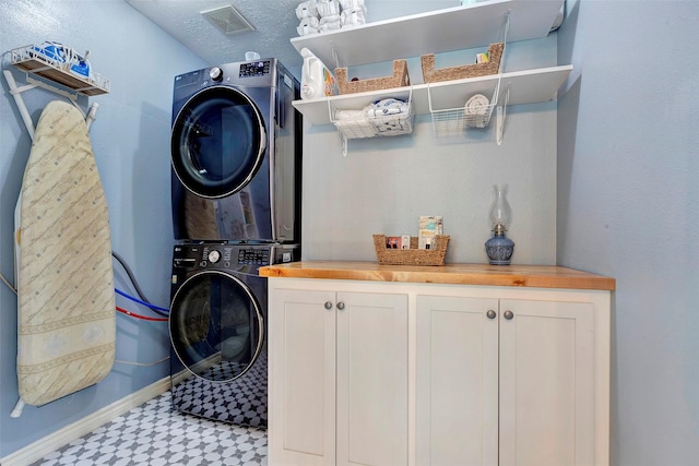 clothes washing area featuring stacked washer / dryer, visible vents, baseboards, cabinet space, and light floors