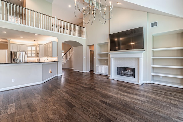 unfurnished living room with baseboards, visible vents, arched walkways, a fireplace with flush hearth, and dark wood-style flooring