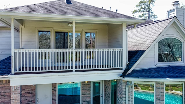 view of home's exterior featuring a shingled roof, brick siding, an outdoor pool, and a balcony