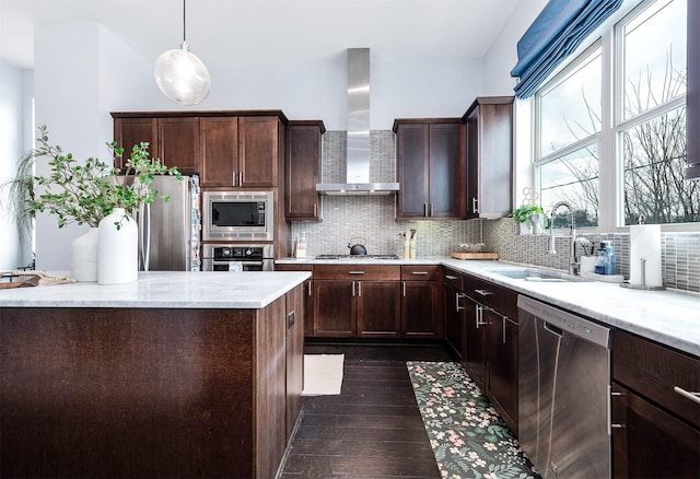 kitchen featuring appliances with stainless steel finishes, tasteful backsplash, wall chimney range hood, and a sink