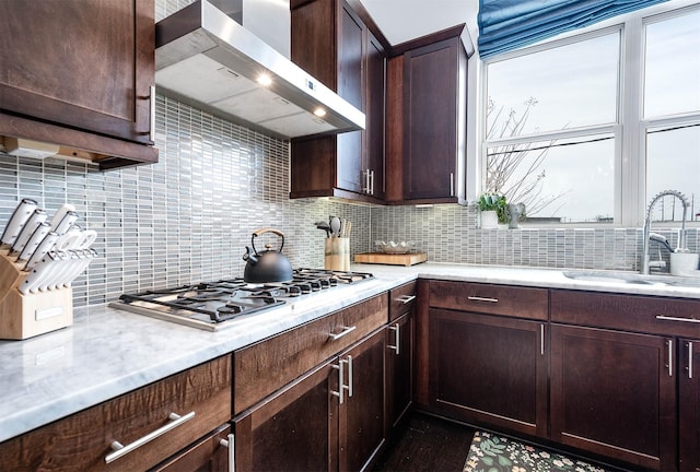 kitchen featuring a sink, stainless steel gas stovetop, dark brown cabinetry, wall chimney exhaust hood, and backsplash