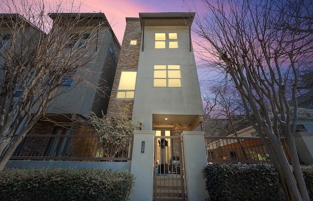 view of front facade featuring stone siding, a fenced front yard, stucco siding, and a gate