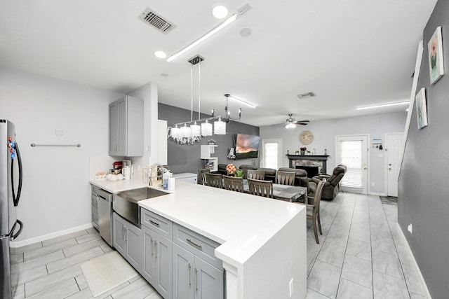 kitchen with gray cabinets, ceiling fan with notable chandelier, decorative light fixtures, sink, and kitchen peninsula