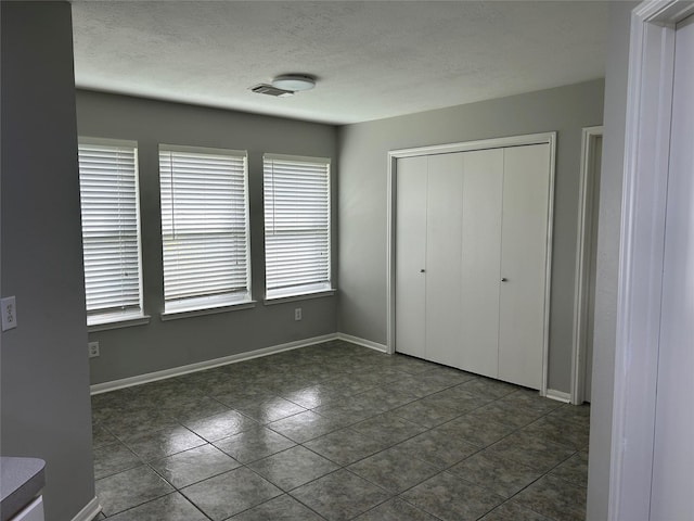 unfurnished bedroom with dark tile patterned flooring, a textured ceiling, and a closet