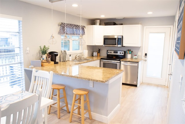 kitchen with sink, stainless steel appliances, white cabinets, decorative light fixtures, and kitchen peninsula